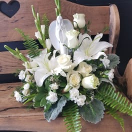 White floral arrangement with lilies and roses on a wooden bench