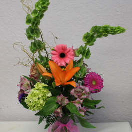 Mixed bouquet with orange lily, pink gerberas, and green hydrangea in a glass vase