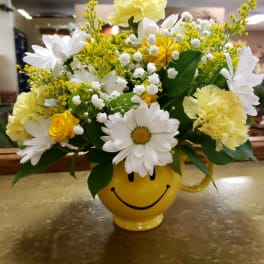 Yellow and white flower arrangement in a smiley-face mug
