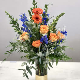 Orange roses and blue flowers in a tall glass vase