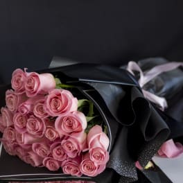 Bouquet of pink roses wrapped in black paper with a pale ribbon