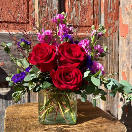 Red roses and purple flowers in a clear glass vase