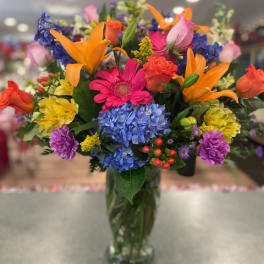 Colorful mixed bouquet in a glass vase with lilies, roses, hydrangeas, and daisies