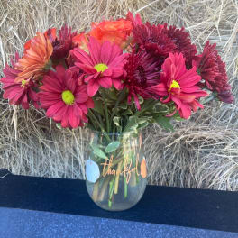 Pink and orange daisy bouquet in a glass vase with a thankful message