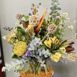 Mixed bouquet with yellow, purple, and white flowers in a low container