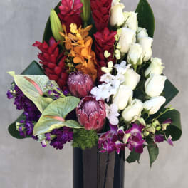 Tropical bouquet with white roses, orchids, and red ginger in a black vase