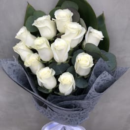 Bouquet of white roses wrapped in dark paper with a lavender ribbon