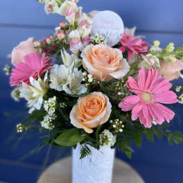 Pink and peach flower arrangement in a white vase with a Mother's Day card