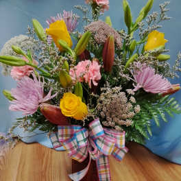 Mixed bouquet with yellow roses, pink lilies, and a plaid ribbon in a vase