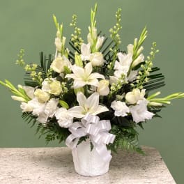 White lilies and carnations in a white vase with a ribbon bow