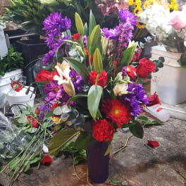 Mixed bouquet with red roses, purple flowers, and white lilies in a tall vase
