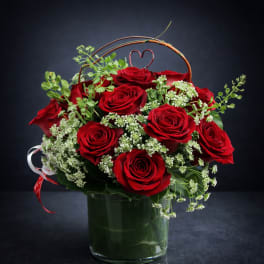 Red roses arranged in a glass vase with white filler flowers and a heart pick