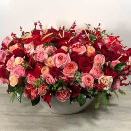 Large pink and red rose arrangement in a white bowl vase