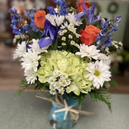 Mixed bouquet with blue, white, and orange flowers in a glass vase