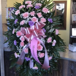 Standing floral spray of pink and purple carnations with a pink ribbon