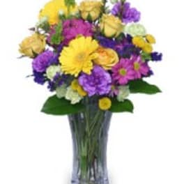 Mixed bouquet of yellow, purple, and pink flowers in a clear glass vase