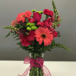 Pink and coral mixed flowers in a glass vase with a pink ribbon