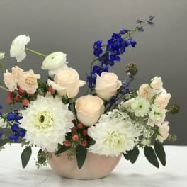 Pastel floral arrangement in a low pink vase with white and blue blooms