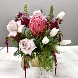 Mixed bouquet with pink protea, pale roses, and white tulips in a gold vase