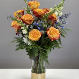 Orange roses with blue and white accent flowers in a glass vase