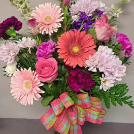 Mixed pink and purple flowers in a glass vase with a plaid ribbon