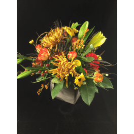 Mixed bouquet of yellow, orange, and red flowers in a square wooden container