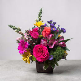Mixed bouquet of bright roses, daisies, and lilies in a dark vase