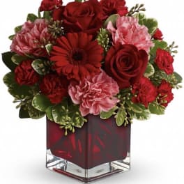 Red and pink flower arrangement in a square glass vase