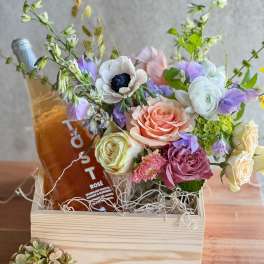 Mixed pastel bouquet in a wooden box with a bottle of rosé