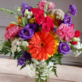 Colorful mixed bouquet in a clear glass vase with orange, pink, purple, and white blooms