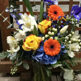 Colorful mixed bouquet in a glass vase with blue irises and orange gerbera daisies