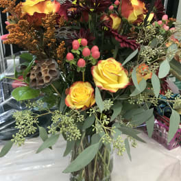 Bouquet of yellow-orange roses in a glass vase with burgundy flowers