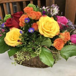 Mixed roses in a low basket arrangement with purple accent flowers