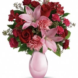 Pink lilies and red roses arranged in a pink glass vase