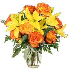 Orange roses and yellow lilies in a clear glass vase