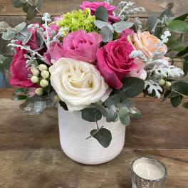 Pink and white roses in a white vase with eucalyptus and a candle nearby