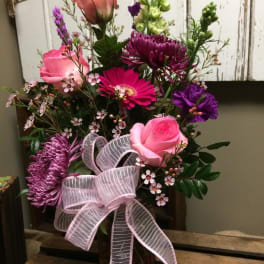 Pink and purple mixed flower arrangement with a ribbon in a glass vase