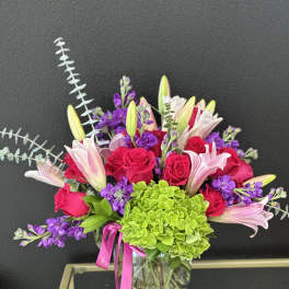 Bouquet of pink roses, lilies, and purple flowers in a glass vase