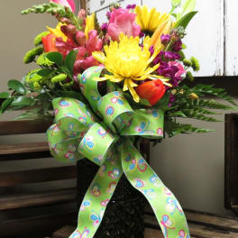 Colorful mixed flower bouquet in a black vase with a green patterned ribbon