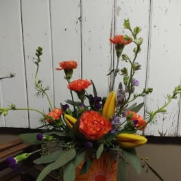 Orange and yellow floral arrangement in a decorative box with tall stems