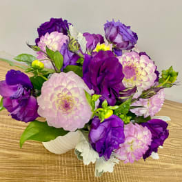 Purple and pink bouquet of dahlias and roses in a white vase
