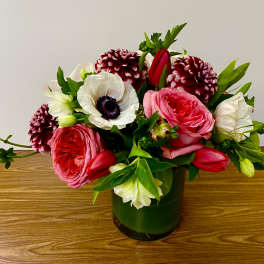Low pink and white flower arrangement with roses, anemones, tulips, and dahlias in a green glass cylinder vase