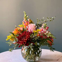 Mixed bouquet of pink, red, and orange flowers in a clear glass vase