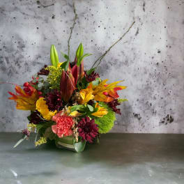 Autumn floral arrangement with lilies, roses, and mums in a low container