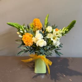 White roses and orange blooms in a green vase with a yellow ribbon