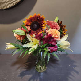 Mixed bouquet with sunflowers, lilies, roses, and pink blooms in a glass vase