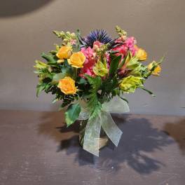 Mixed bouquet of yellow roses, pink blooms, and blue thistle in a glass vase