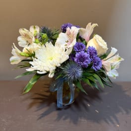 White and purple mixed bouquet in a glass vase with a blue ribbon