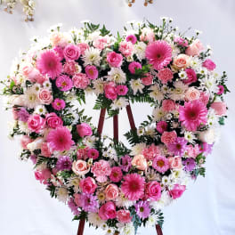 Heart-shaped floral wreath with pink roses and white daisies on an easel