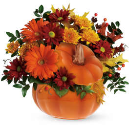 Autumn floral arrangement in an orange pumpkin container with red and yellow flowers